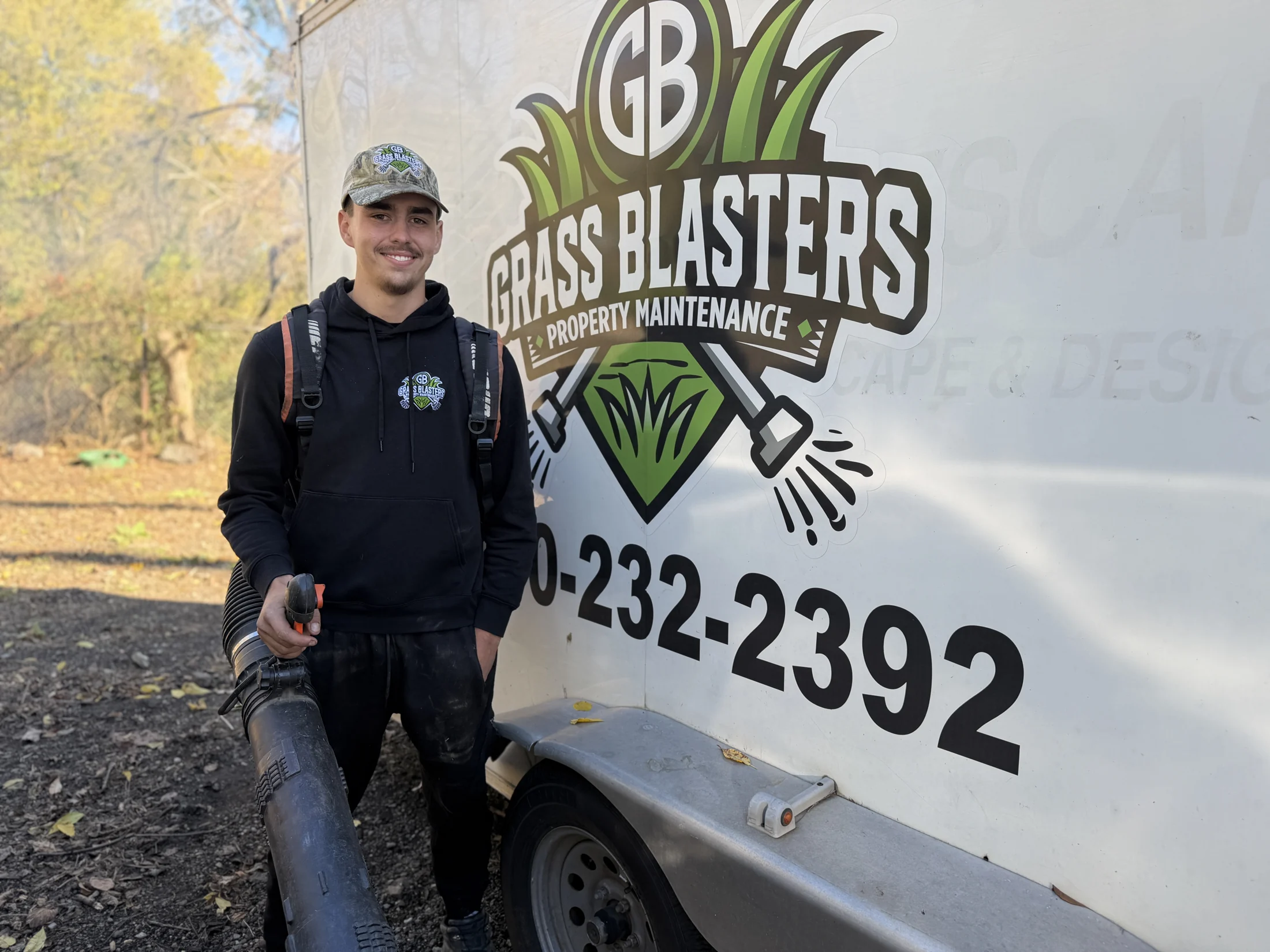 Grass Blasters team member with a leaf blower beside the branded trailer